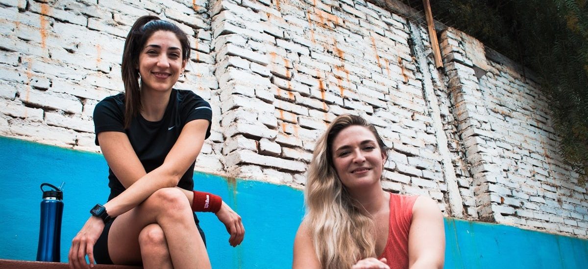 two women sitting on a wall with a brick wall behind them