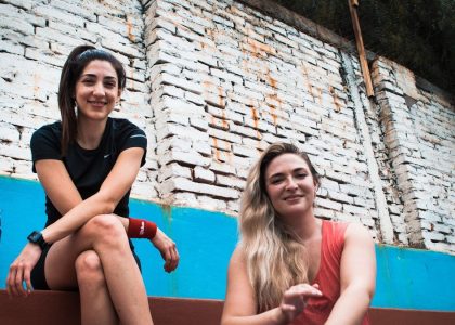 two women sitting on a wall with a brick wall behind them
